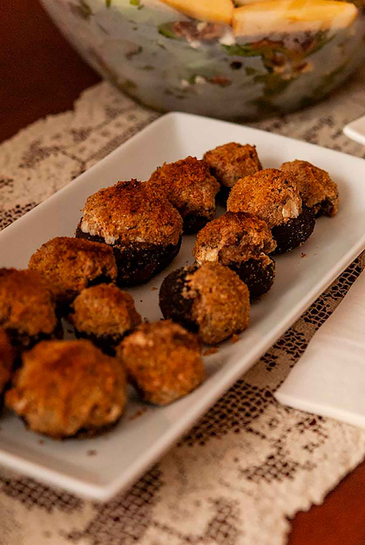 A plate of stuffed mushrooms on a table with an old, lace tablecloth.