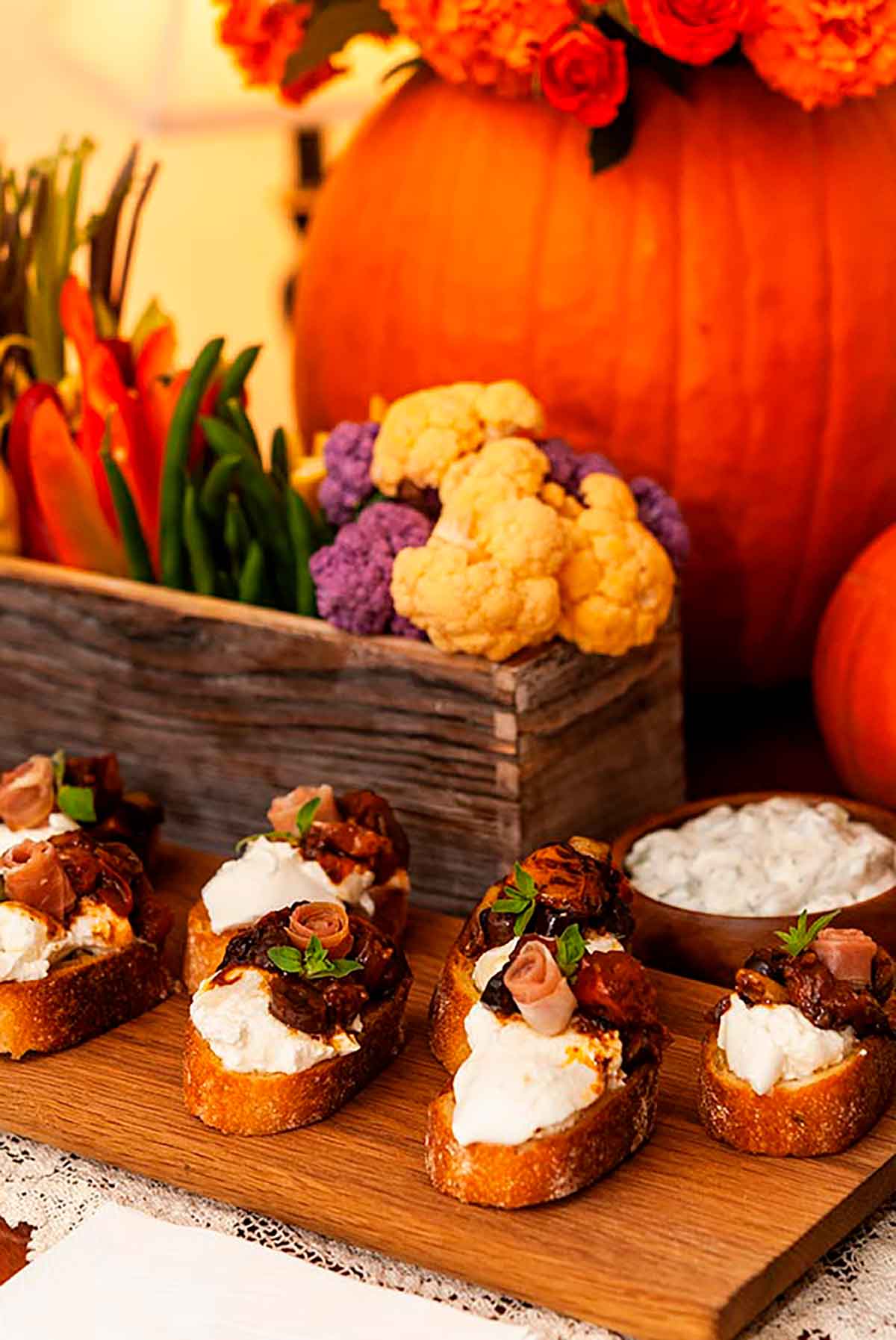 7 bruschetta, garnished with prosciutto roses on a wooden board and a flower-box crudités in front of a pumpkin.