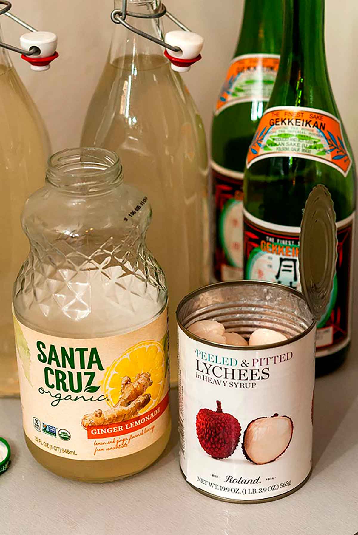 Sake, bottles of pre-mixed cocktails, a bottle of ginger lemonade and an open can of lychees on a table.