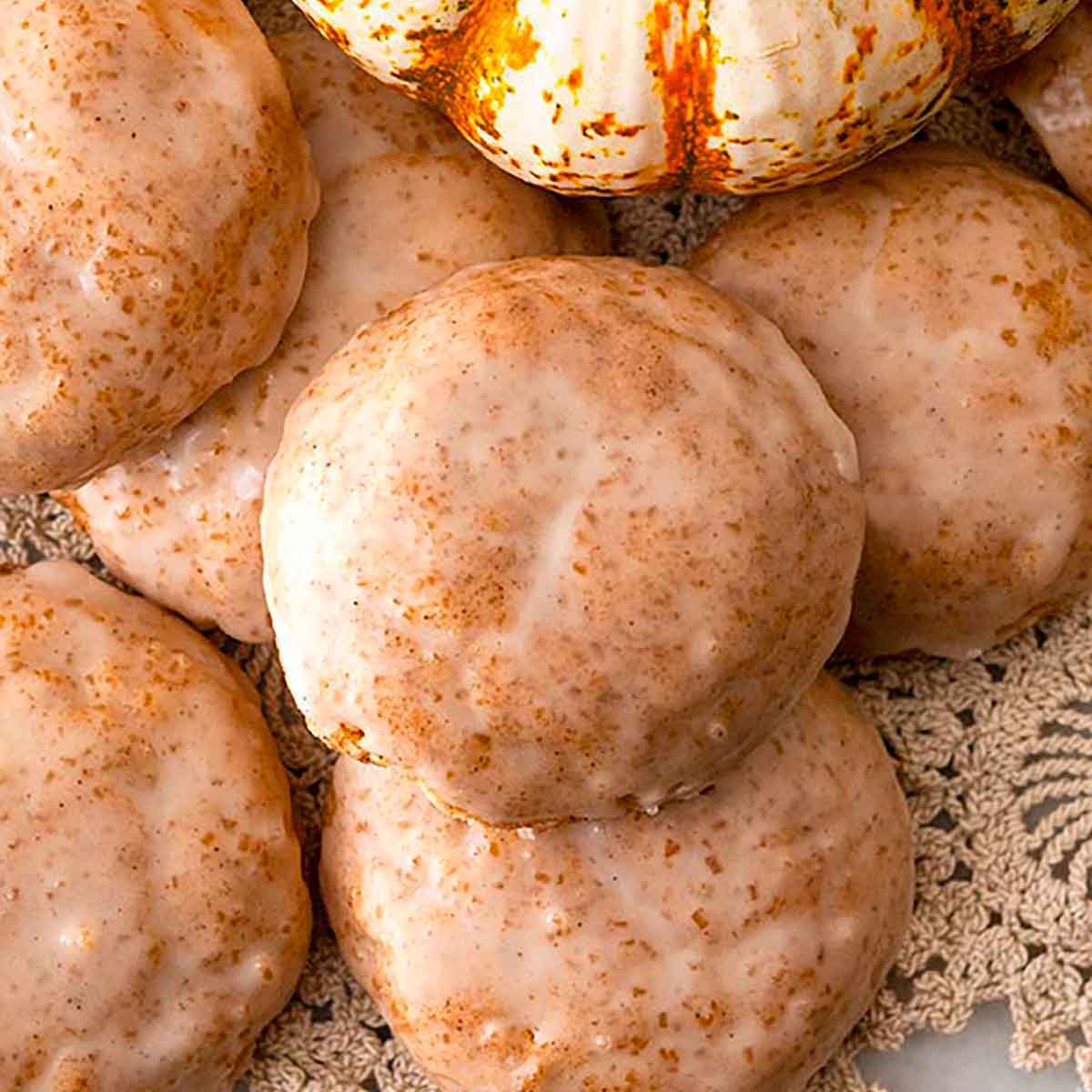 7 glazed cookies on lace, beside a pumpkin gourd.