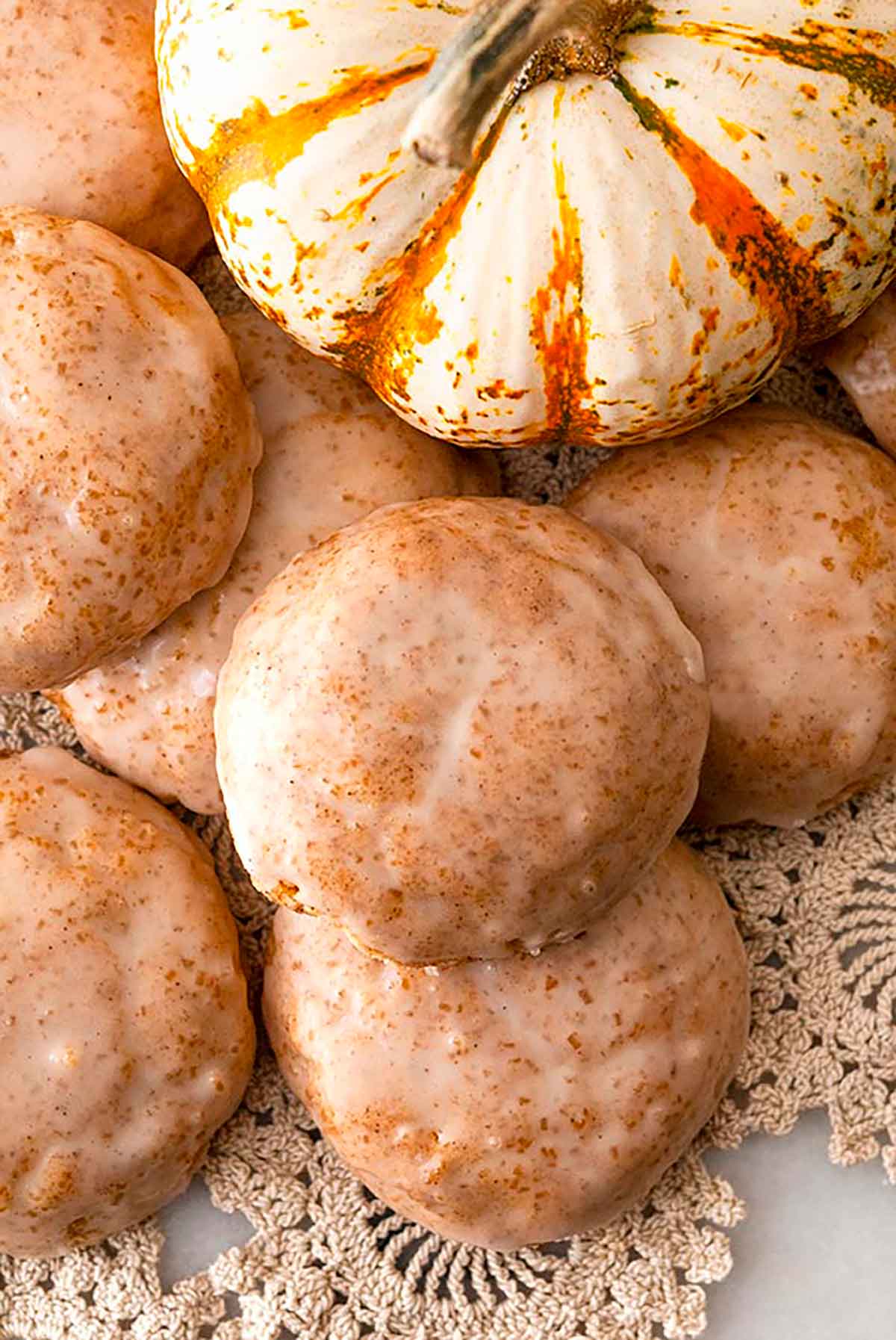 7 glazed cookies on lace, beside a pumpkin gourd.