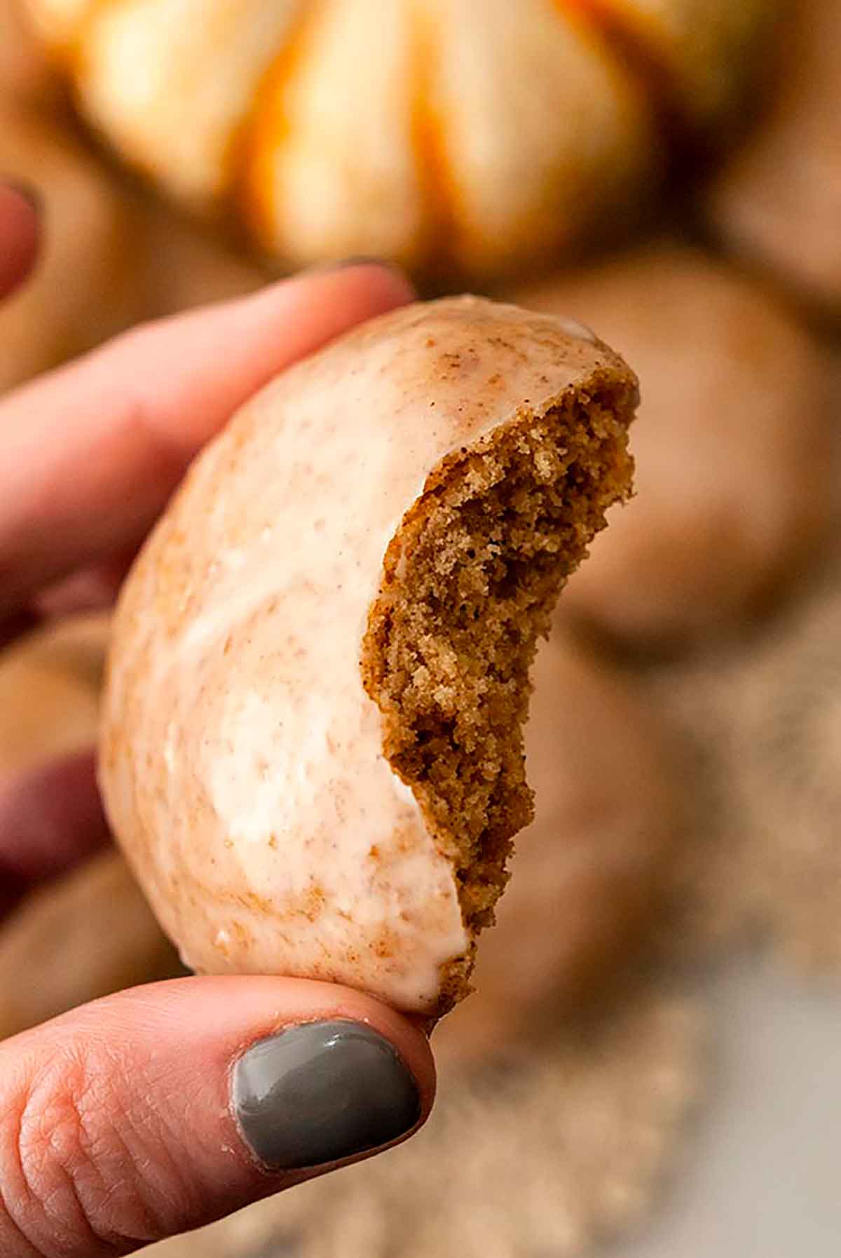 Fingers holding a bitten, glazed cookie above a pile of others.