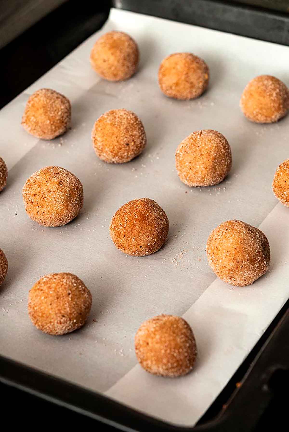 16 balls of sugar-coated dough on a parchment-lined baking pan.