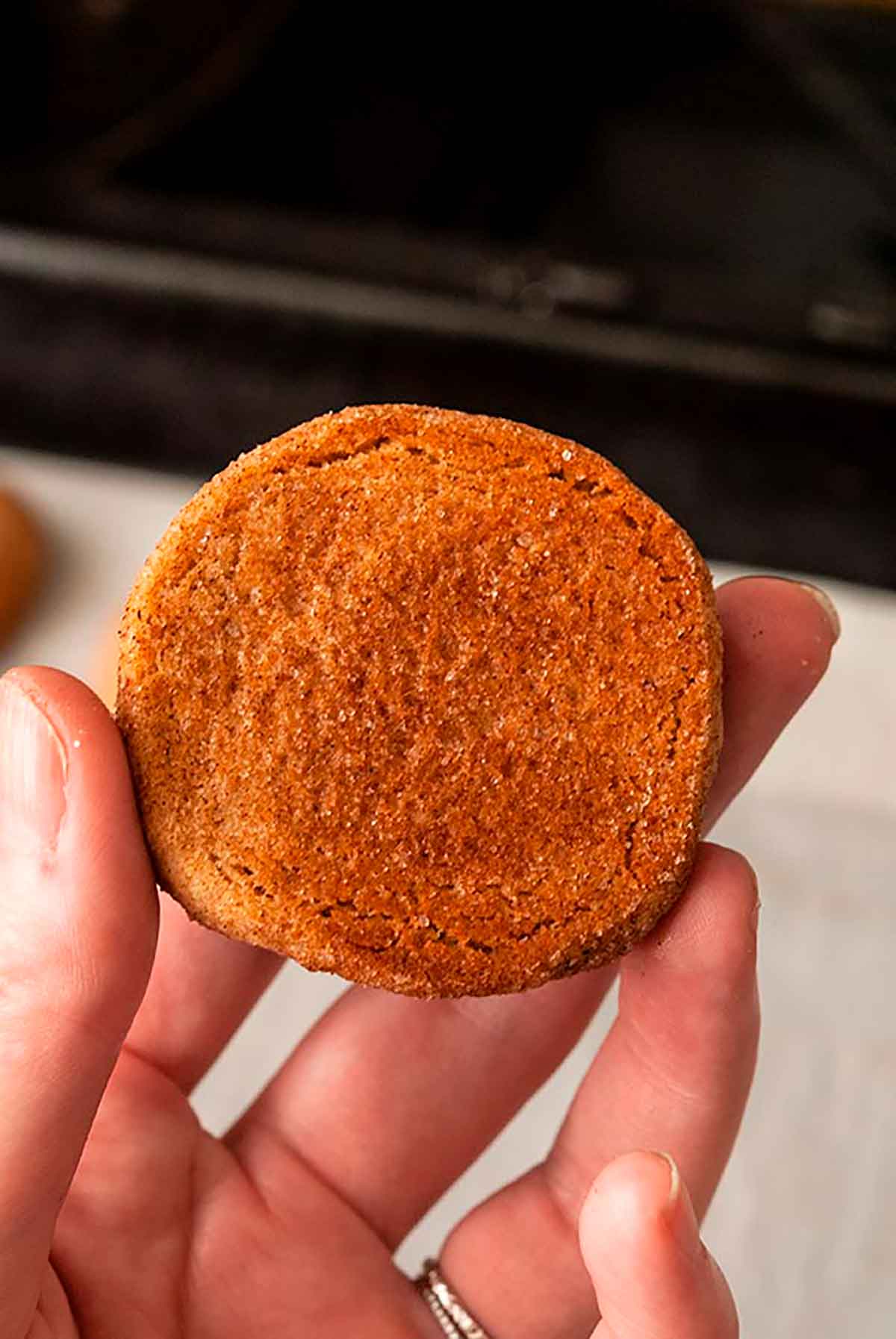 Fingers holding a snickerdoodle showing the brown bottom above a baking pan.