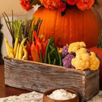 A flower box crudités on a table in front of a pumpkin full of flowers.