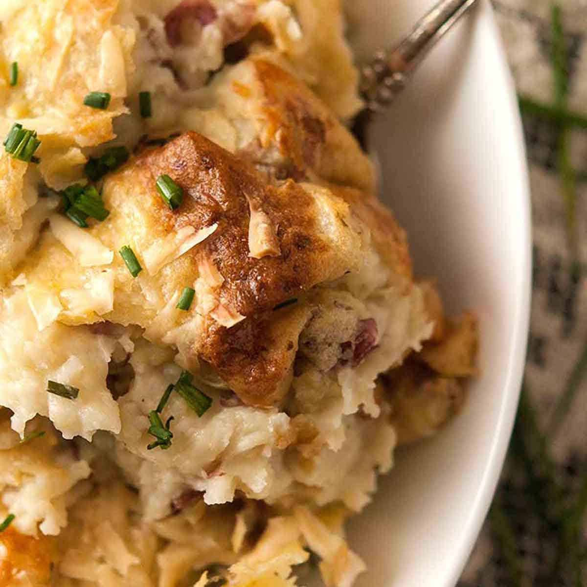 A bowl of baked mashed potatoes on a table with a lace tablecloth.