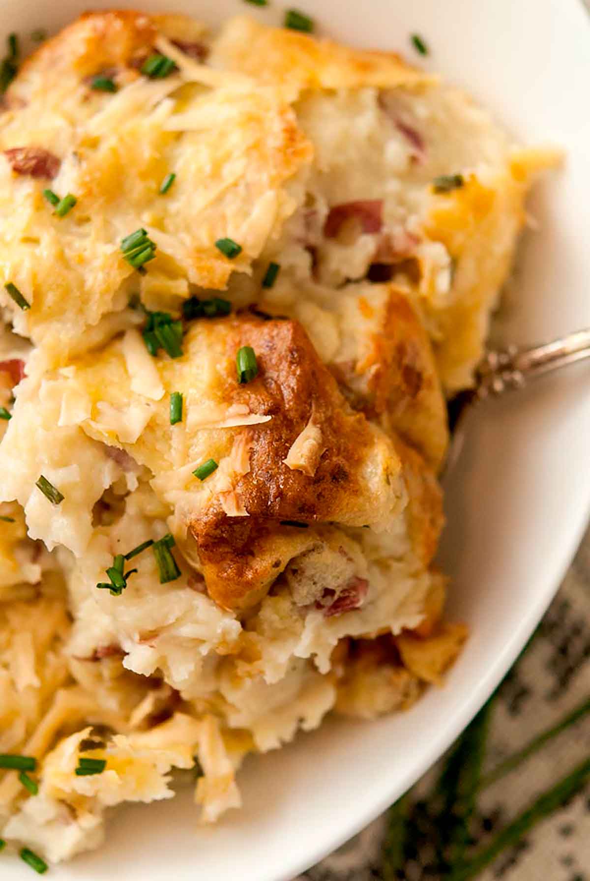 A bowl of baked mashed potatoes on a table with a lace tablecloth.