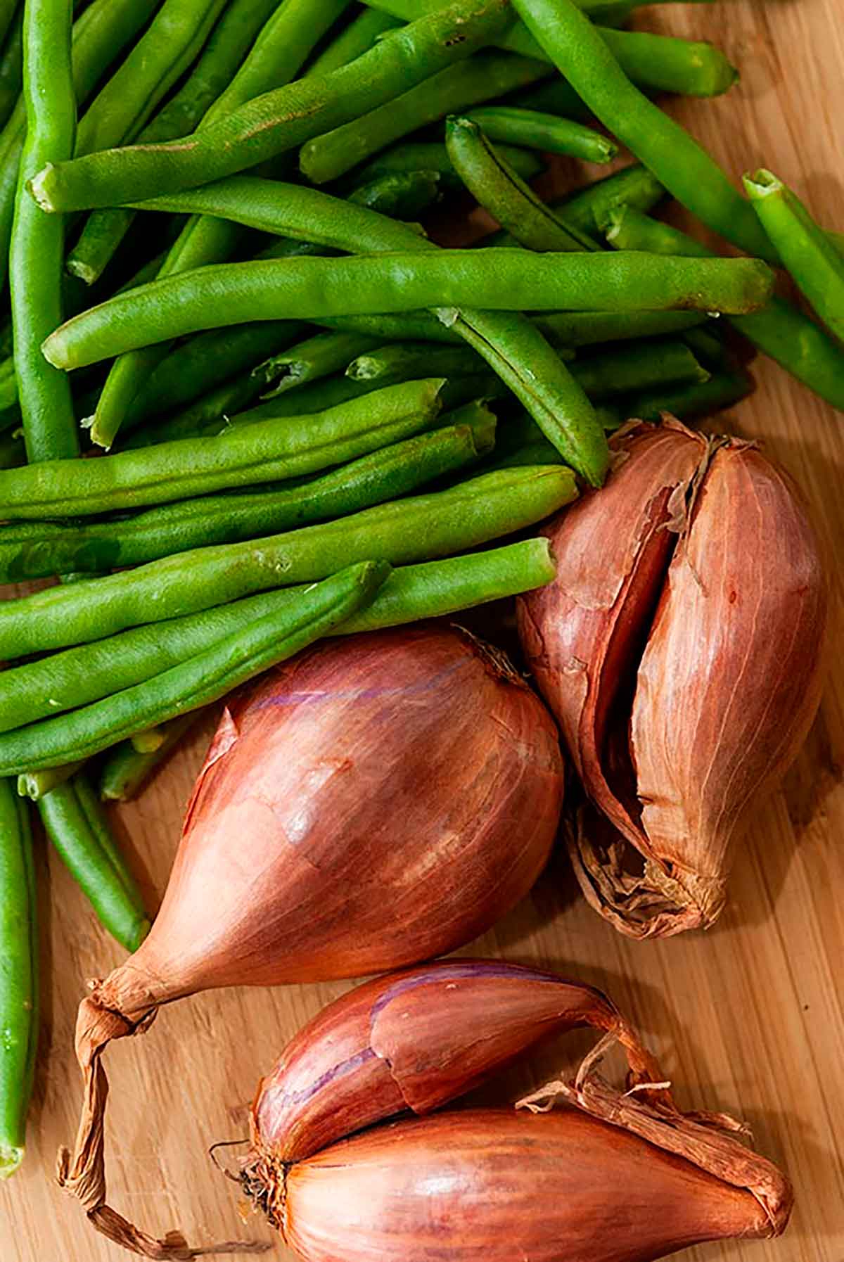 Uncooked shallots and green beans on a cutting board.