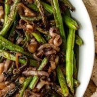 A bowl of french green beans with cooked shallots.