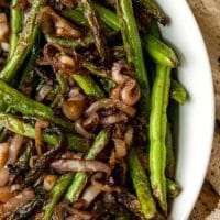 A bowl of french green beans with cooked shallots.