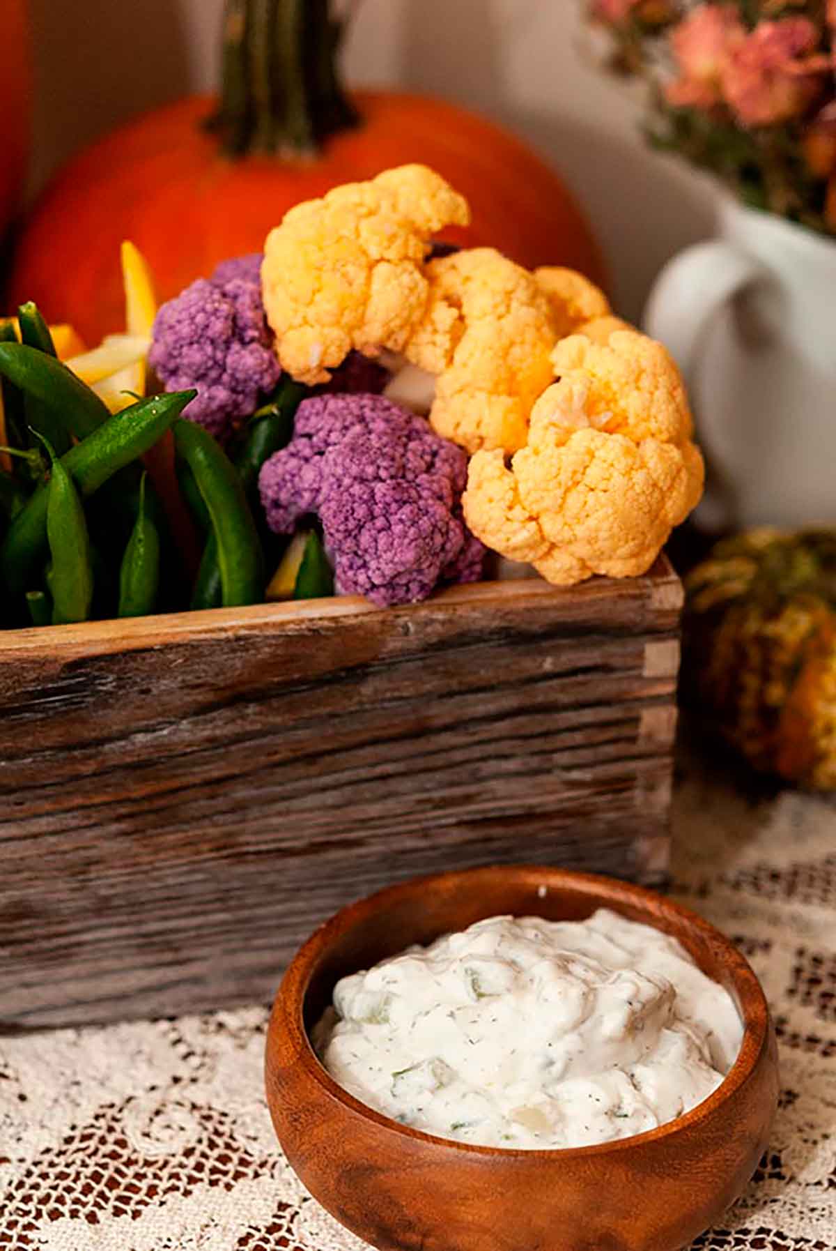 A small wooden bowl of vegetable dip in front of a flower box full of vegetables.