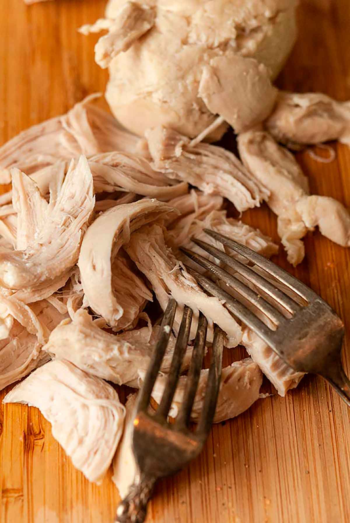 2 forks pulling apart cooked chicken on a cutting board.