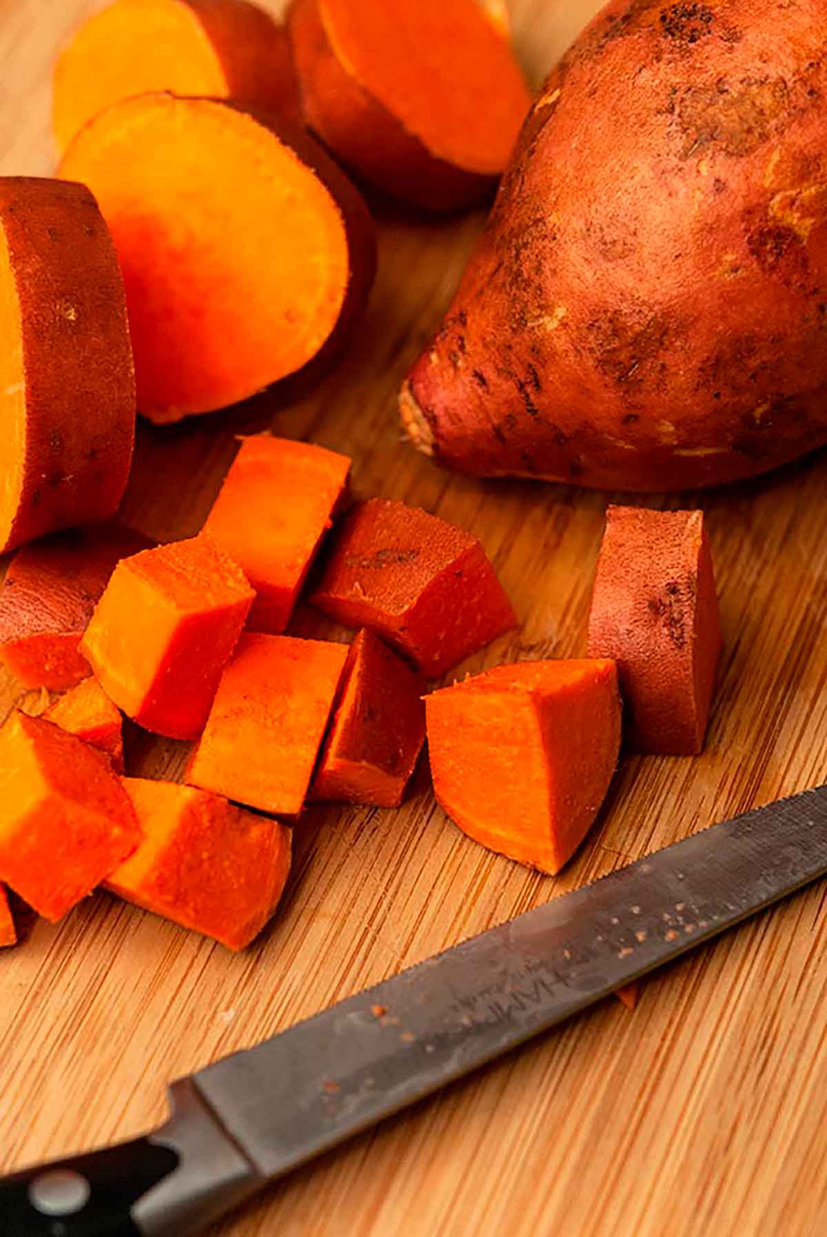 A diced sweet potato on a cutting board with a knife.