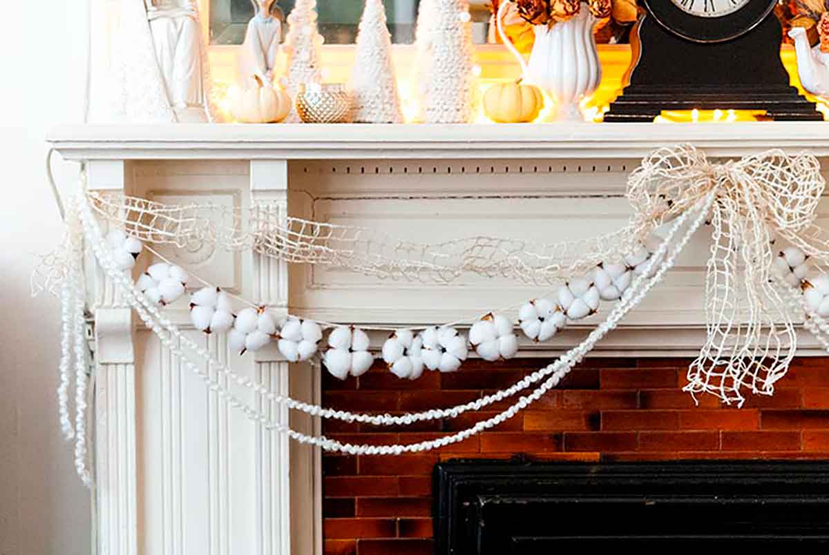 Cotton garland strung on a mantle with yarn and ribbon, with various Christmas decorations on the mantle top.