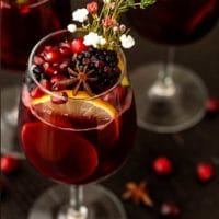 A glass of sangria garnished with fruits, flowers, herbs and star anise on a dark table.