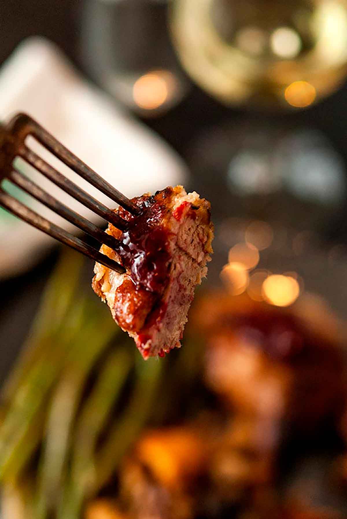 A fork holding a slice of duck meat with blackberry sauce.