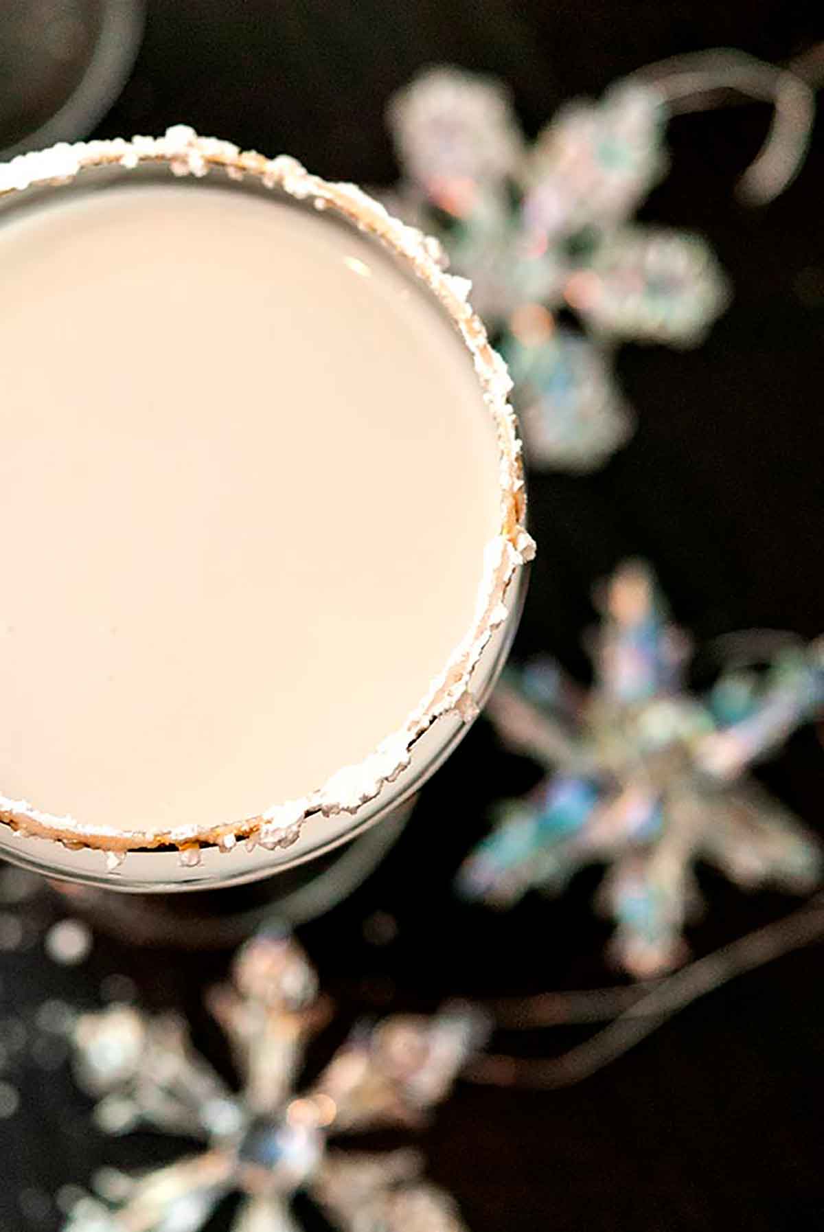 A white cocktail, rimmed with powdered sugar, on a black table, sprinkled with sugar and with a few snowflake ornaments.