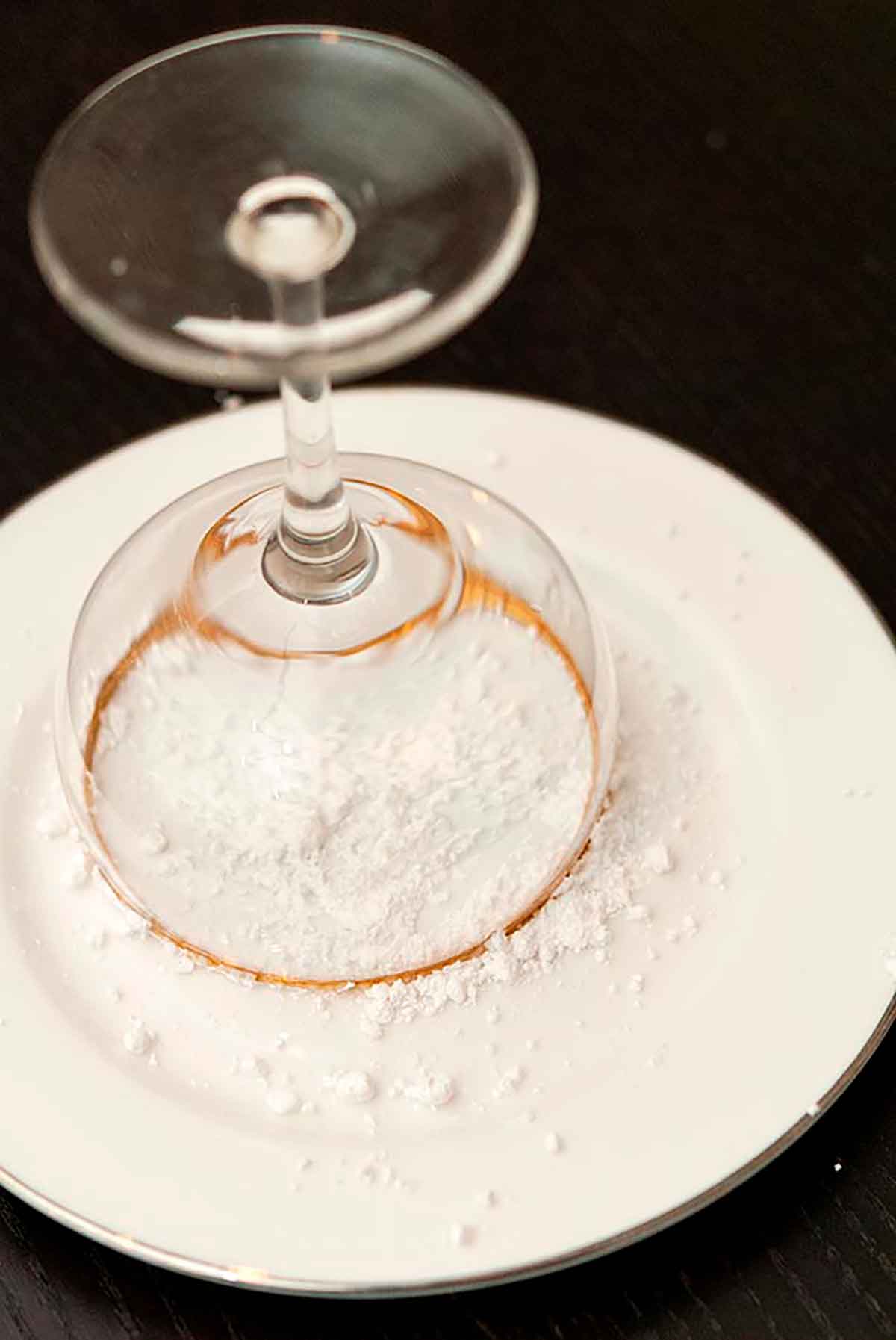 A cocktail glass pressed into powdered sugar on a white plate.
