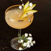 A pear and ginger cocktail, garnished with sliced pears on a cocktail pin and a few baby's breath flowers.