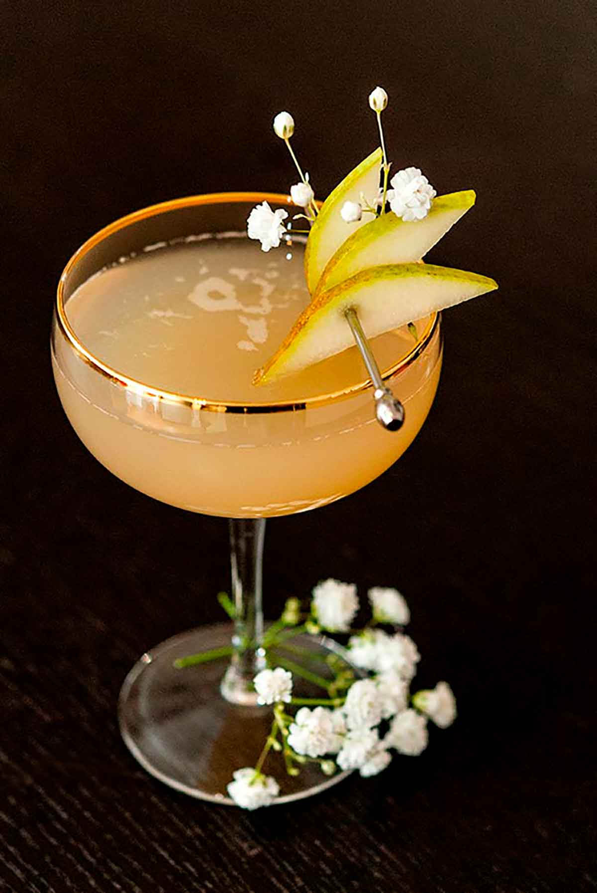 A pear and ginger cocktail, garnished with sliced pears on a cocktail pin and a few baby's breath flowers.