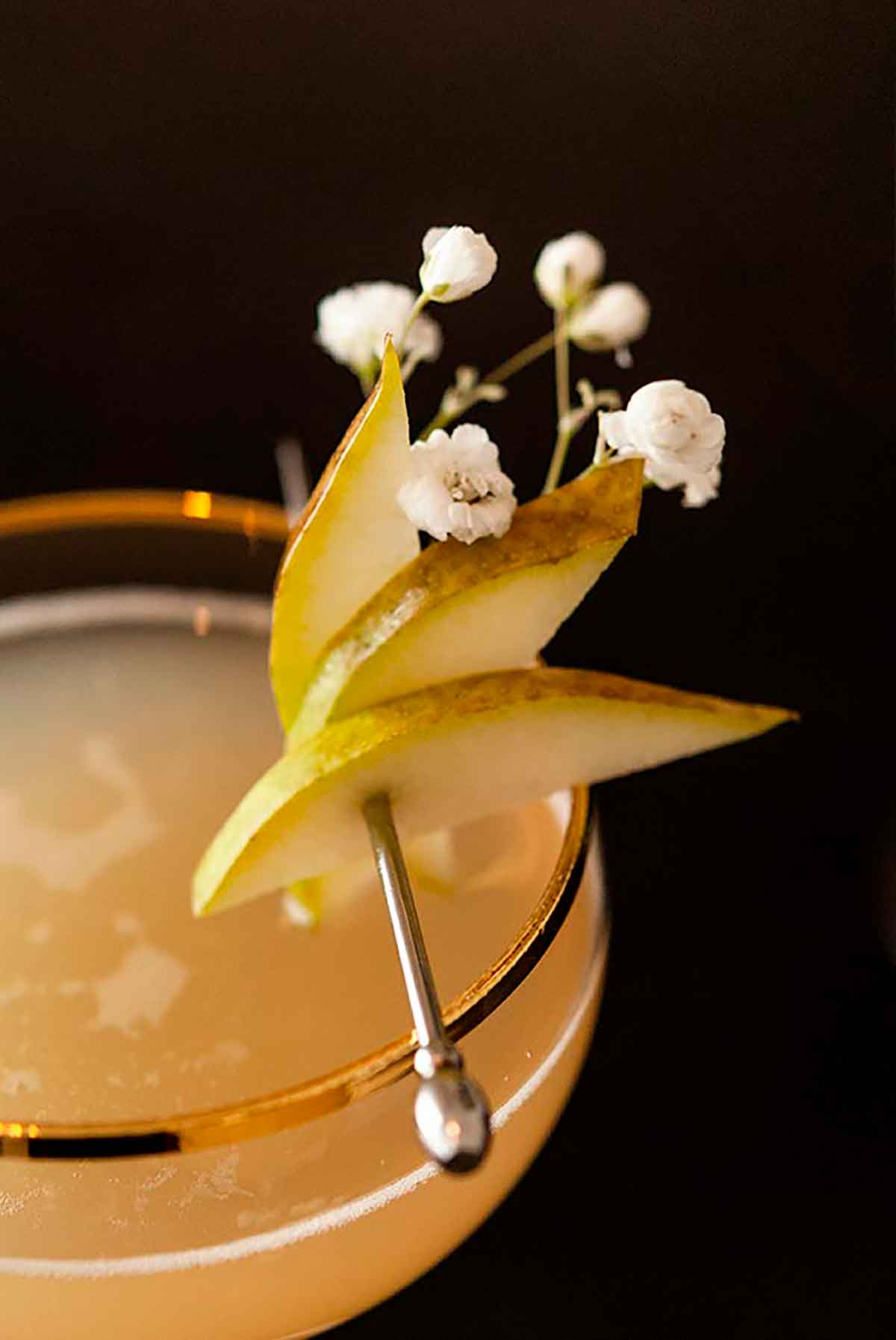 The garnish on a pear & ginger cocktail. It is 3 pear slices on a cocktail pin with a few baby's breath flowers.