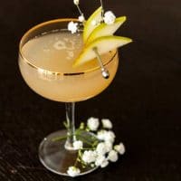 A pear and ginger cocktail, garnished with sliced pears on a cocktail pin and a few baby's breath flowers.