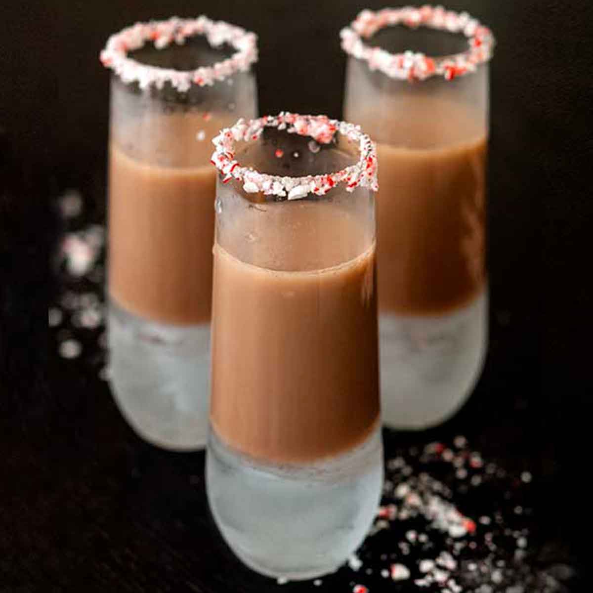 3 chocolate cocktails, rimed with crushed candy cane on a black table.