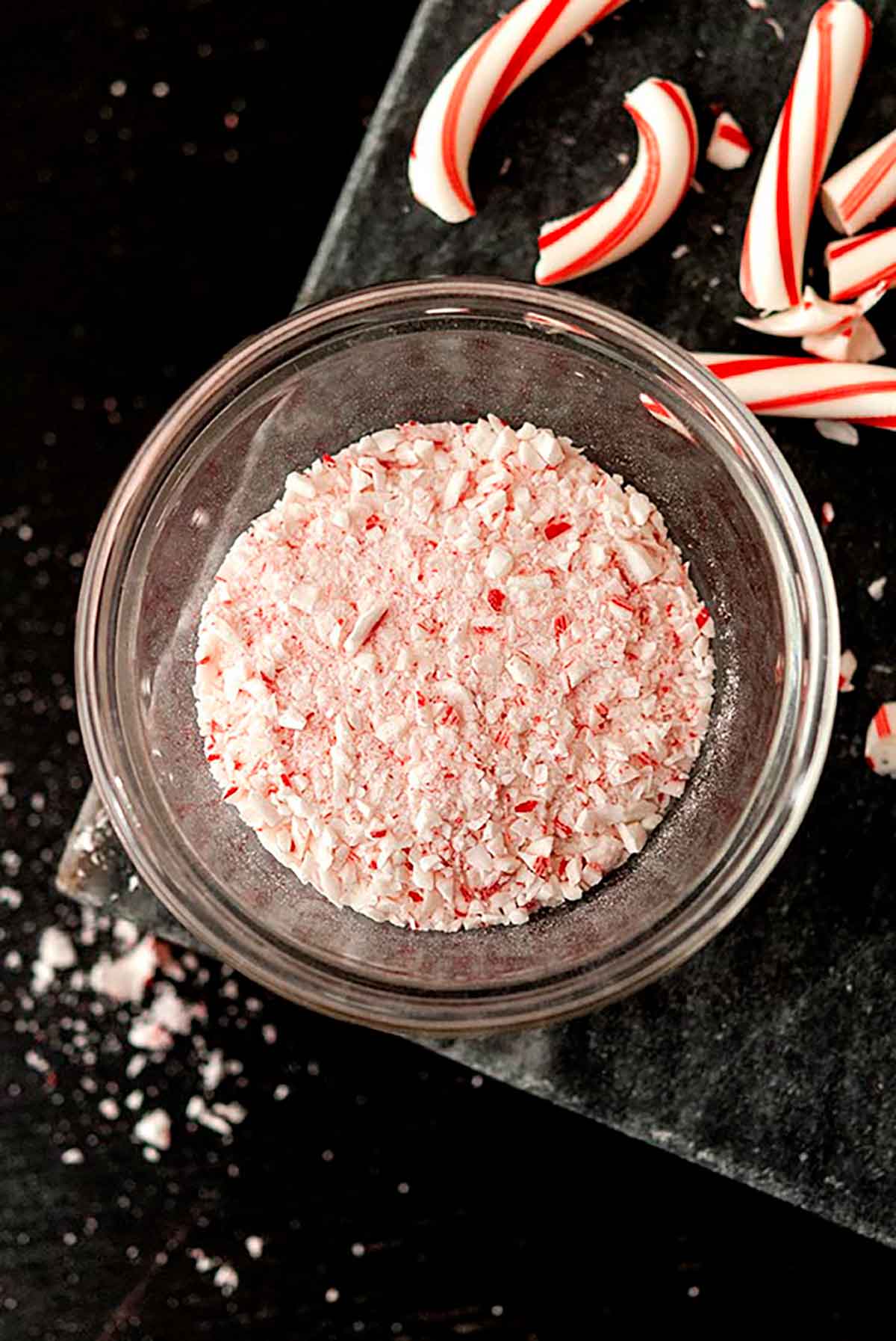 Crushed candy cane powder in a bowl on a table with broken candy canes.