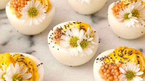 10 deviled eggs on a marble plate garnished with daisies and mustard caviar.