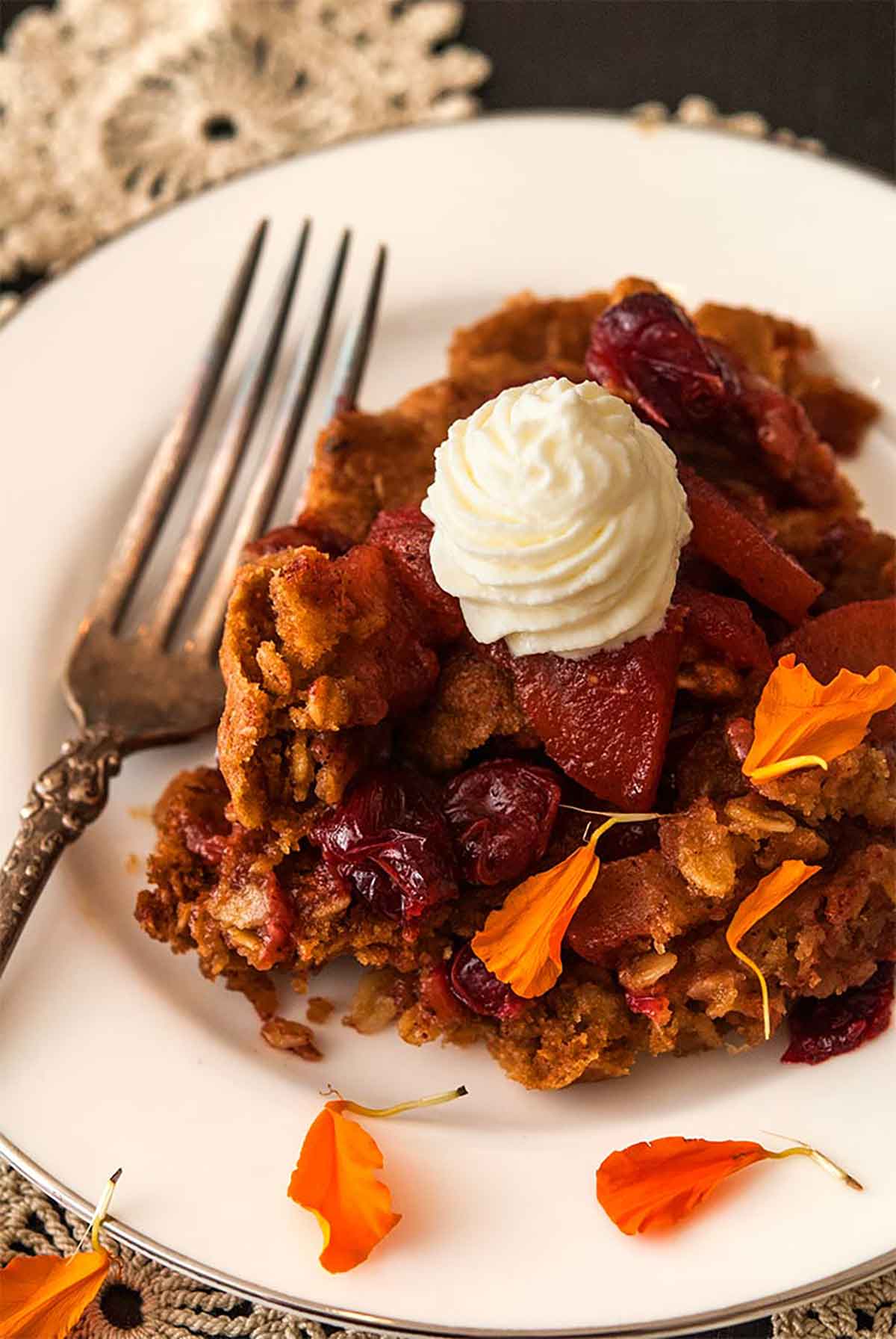 Cranberry apple crisp on a plate, topped with whipped cream and sprinkled with marigold flower petals.