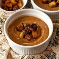 A bowl of cauliflower soup on a lace table cloth in front of 2 others.