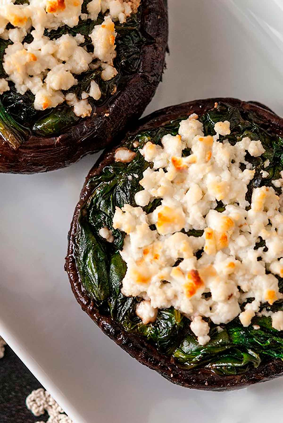 The top of 2 stuffed mushrooms with spinach and toasted feta on top, sitting on a plate.