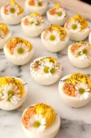 12 deviled eggs on a marble plate garnished with daisies and mustard caviar.