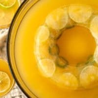 A bowl of pineapple punch in a punch bowl, with an ice ring filled with limes and jalapeños in the center.