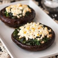 2 spinach and feta-stuffed mushroom caps on a white plate on a table, lined with lace with 2 plates in the background.