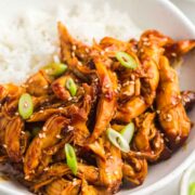 A bowl of teriyaki chicken in a bowl with white rice on a table.