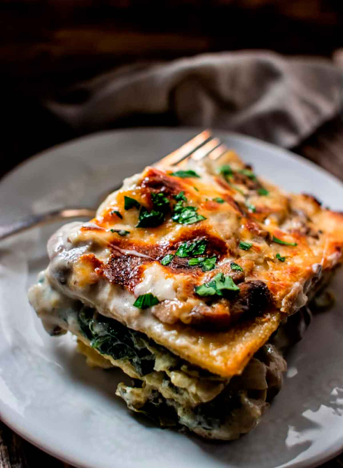 A slice of mushroom, spinach and artichoke lasagna on a plate.