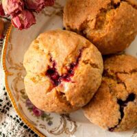 3 lemon-raspberry scones on an antique plate, beside a few dry, pink spray roses.