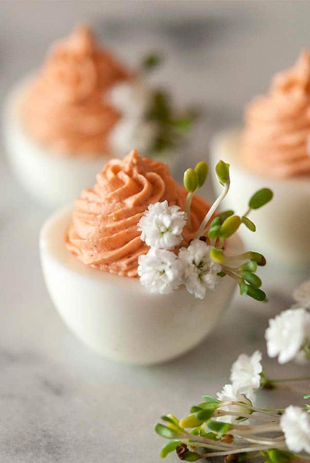 3 deviled eggs on a marble table with pink filling and garnished with baby's breath and sprouts.