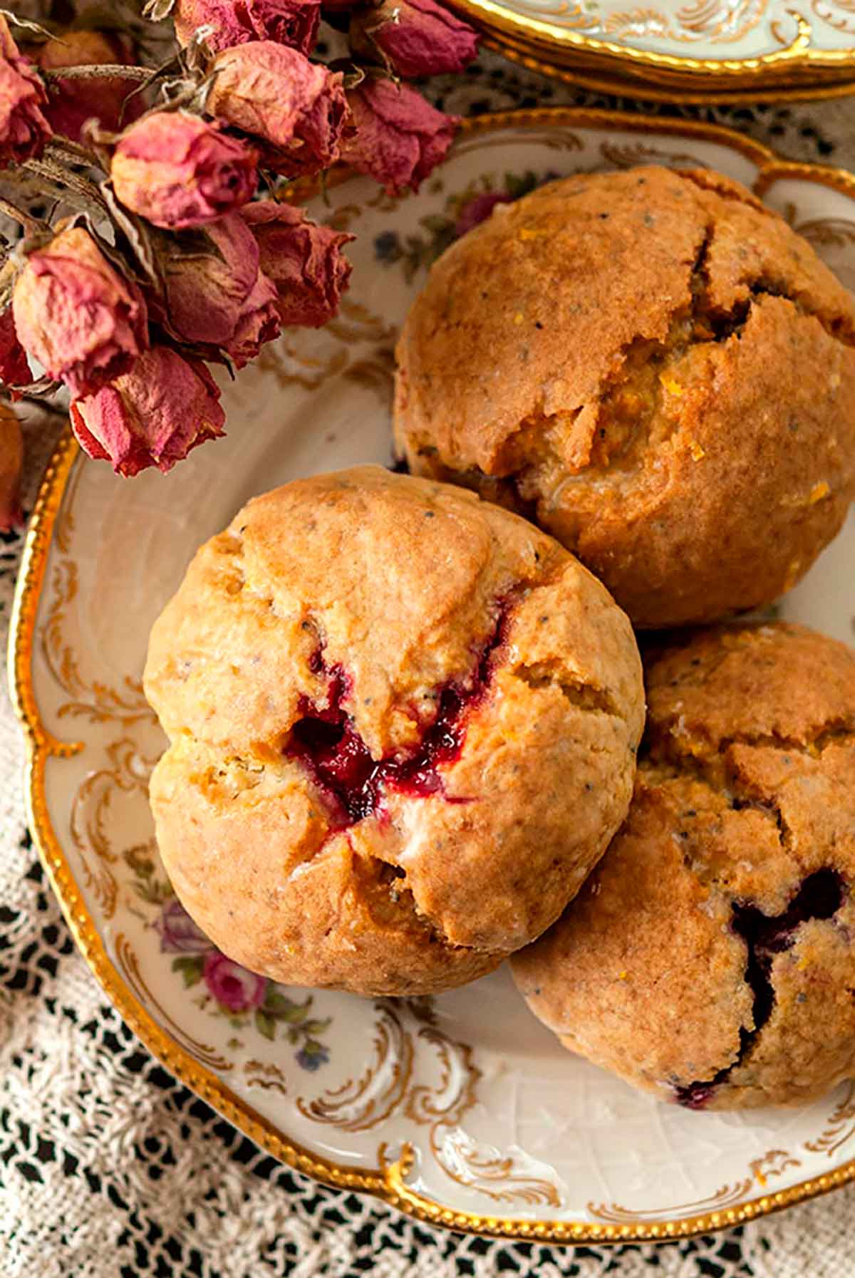 3 lemon-raspberry scones on an antique plate, beside a few dry, pink spray roses.