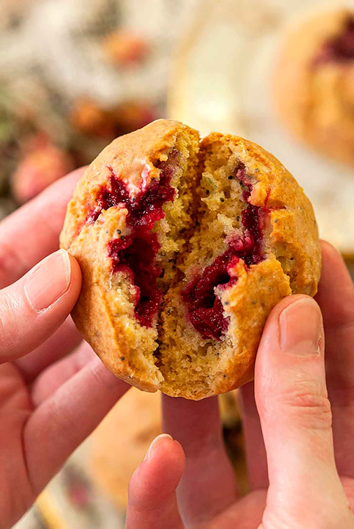 Hands opening up a scone showing raspberries inside.