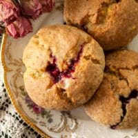 Glazed raspberry lemon poppyseed scones on a plate beside dry roses.