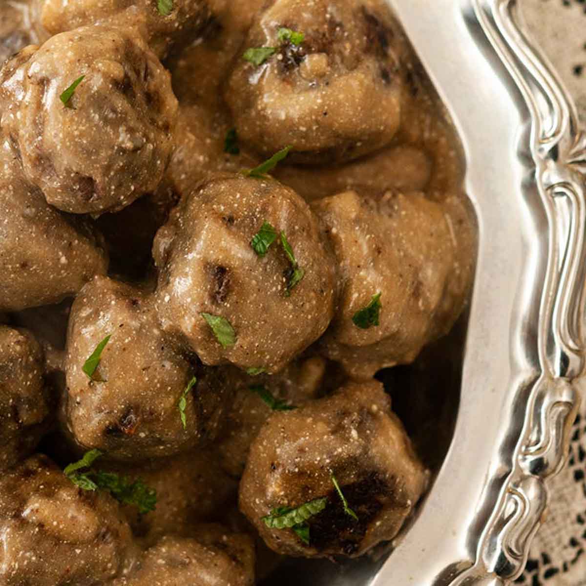 Swedish meatballs in a silver bowl on a lace tablecloth.