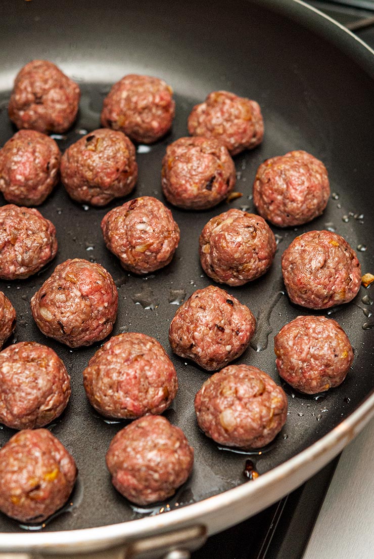 20 raw meatballs in a skillet.