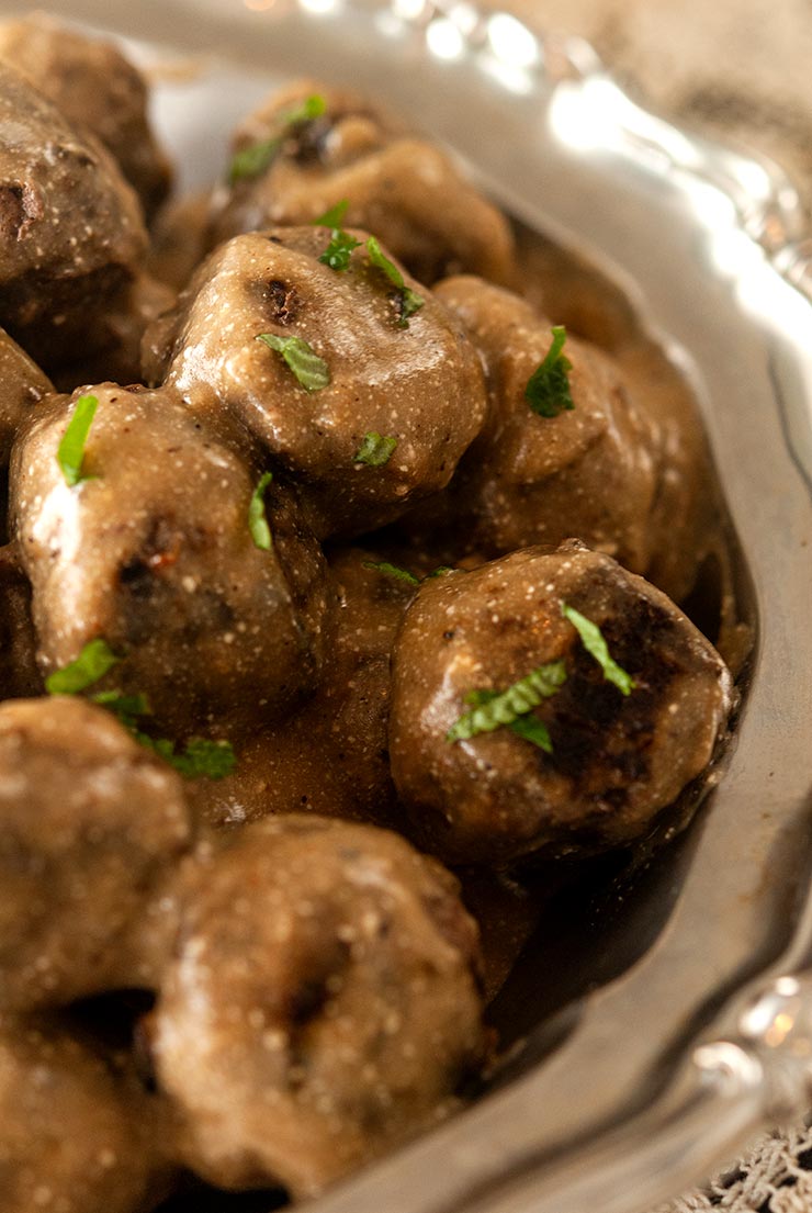 Swedish meatballs in a silver bowl on a lace tablecloth.