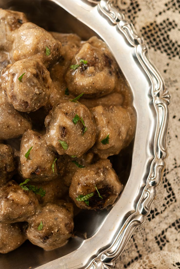 Swedish meatballs in a silver bowl on a lace tablecloth.