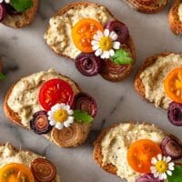 Crostini garnished with daisies, onions and tomatoes on a marble plate