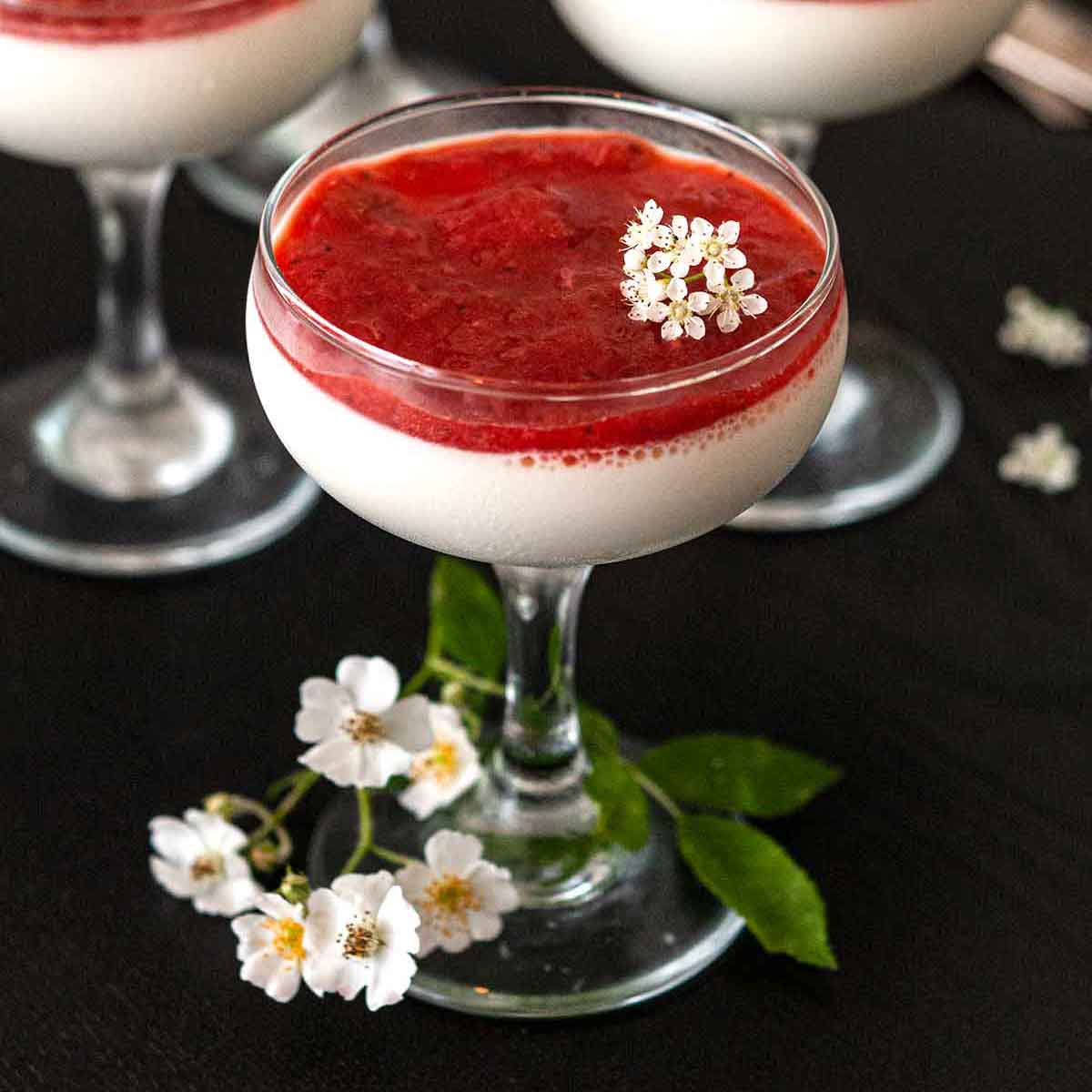 A glass of panna cotta with strawberry-rhubarb compote, garnished with flowers, on a table.