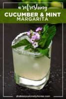 A cucumber mint margarita, garnished with small flowers and mint, on a table lightly sprinkled with salt.