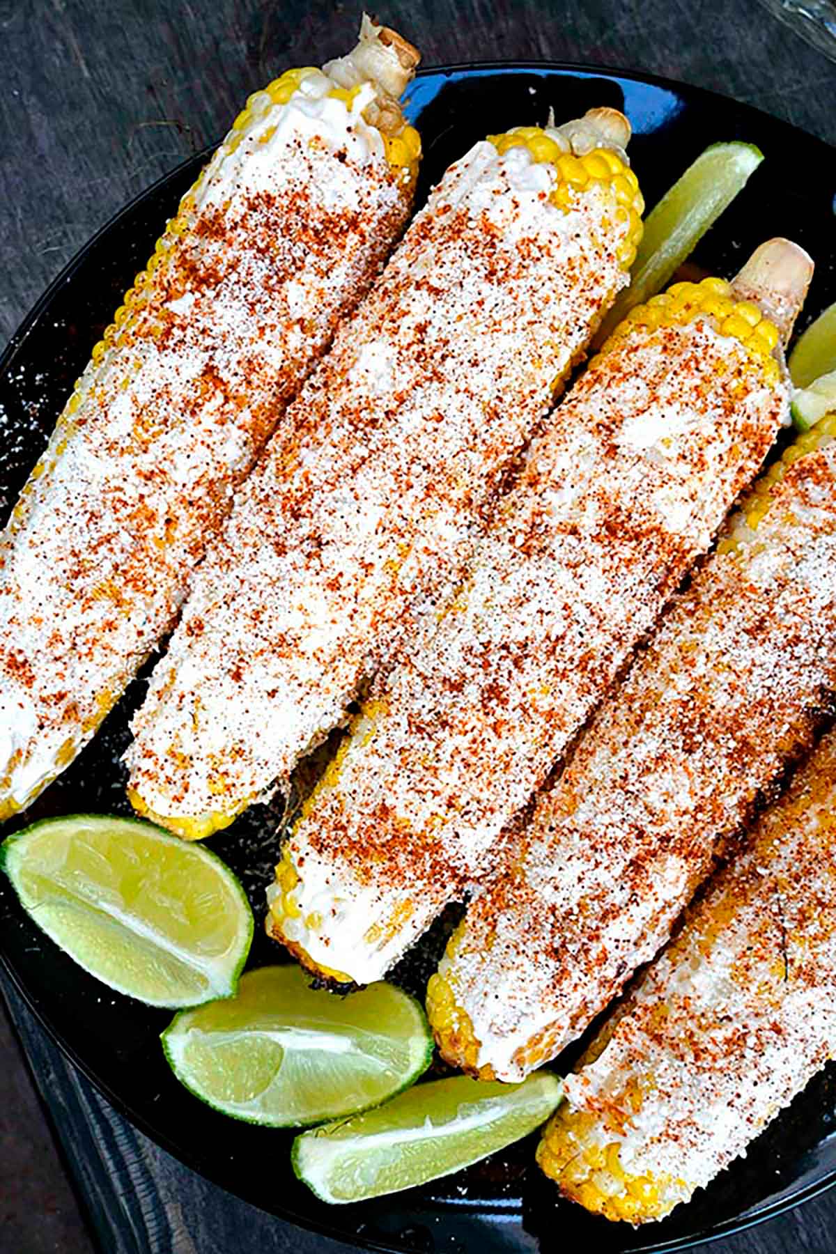 Elote (spiced and cheese-sprinkled corn) on a plate with 4 lime wedges.